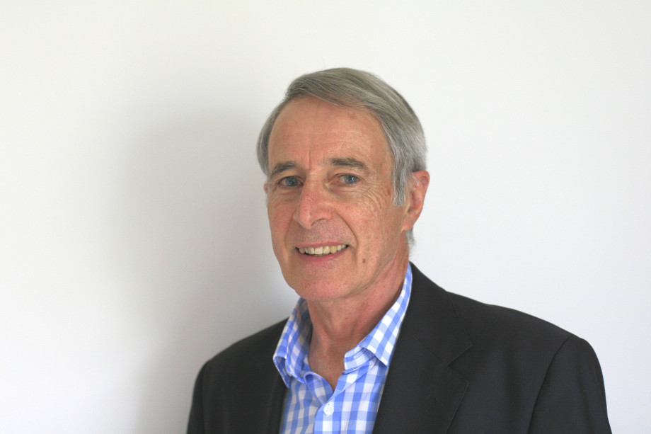 Greg Ayers, wearing a dark suit and blue and white shirt, smiles at the camera.