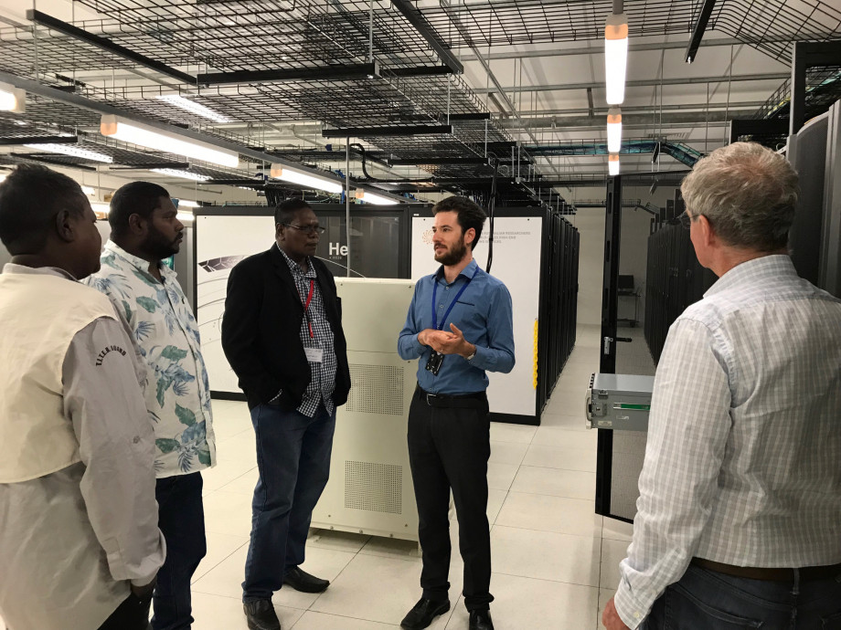 A group of Indigenous people standing with a tour guide giving them a tour of a supercomputer.