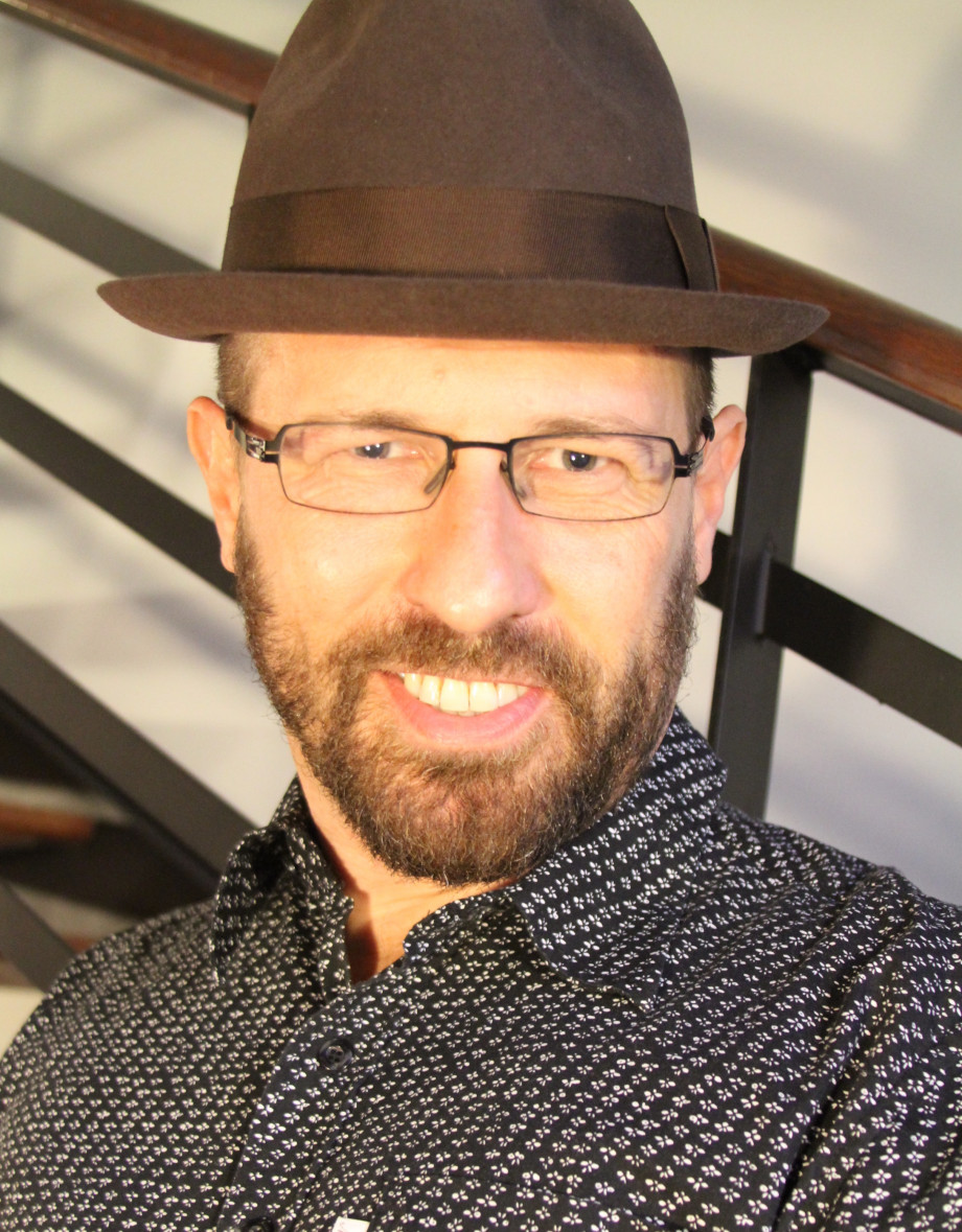 A bearded man wearing a hat smiling at the camera.