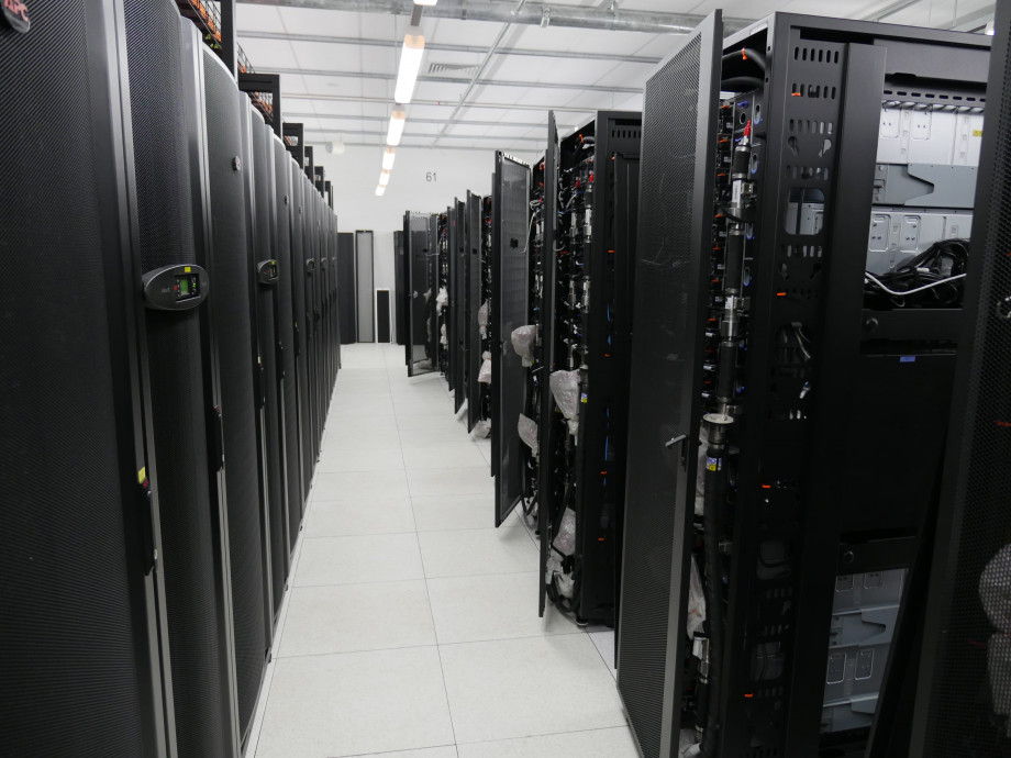 A solid row of black server racks on the left facing new, unconnected server racks on the right.