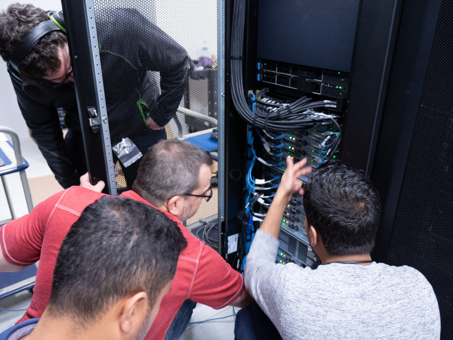 Computer experts huddle around computing equipment.