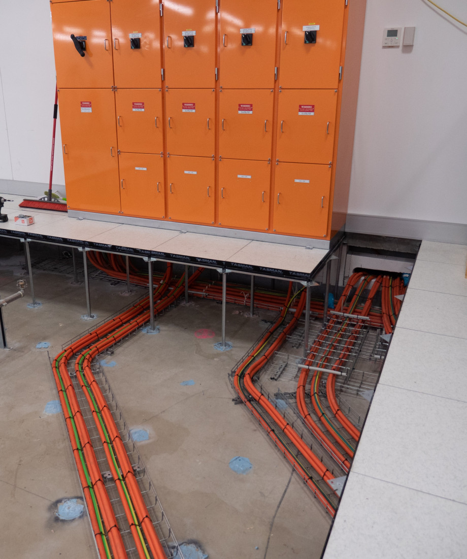 Neatly lined up orange cables in bundles run on the exposed concrete slab to connect underneath an orange electrical box.