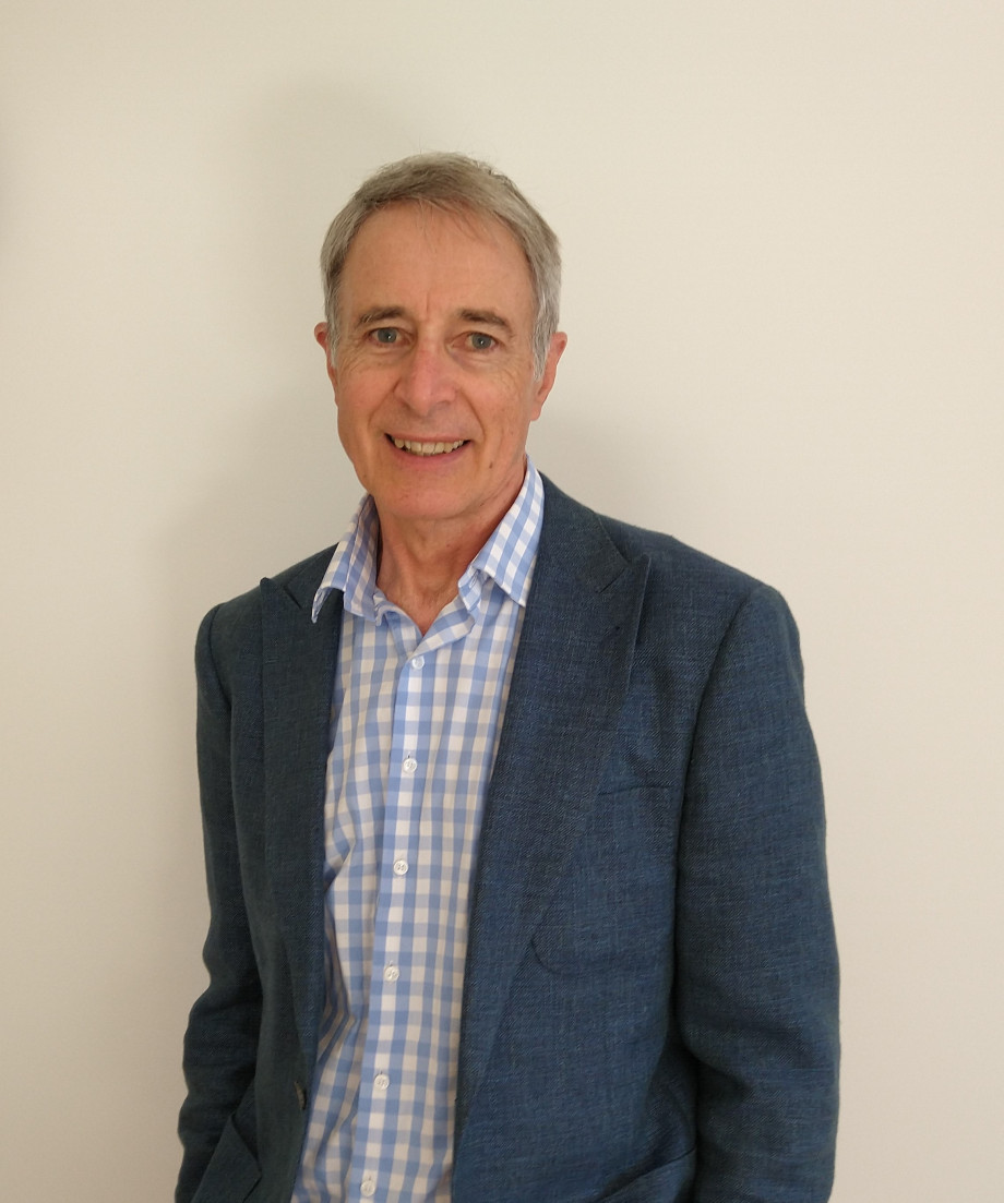 A smiling man wearing a blue suit and blue and white checkered shirt.