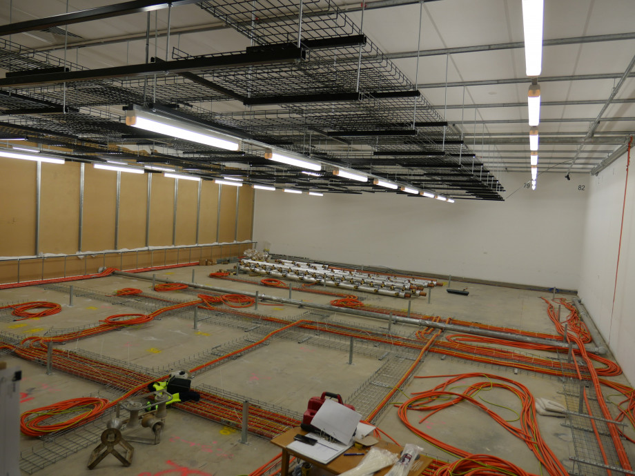 A concrete floor covered with neatly arranged orange electrical cables, and some metal pipes lined up in rows.