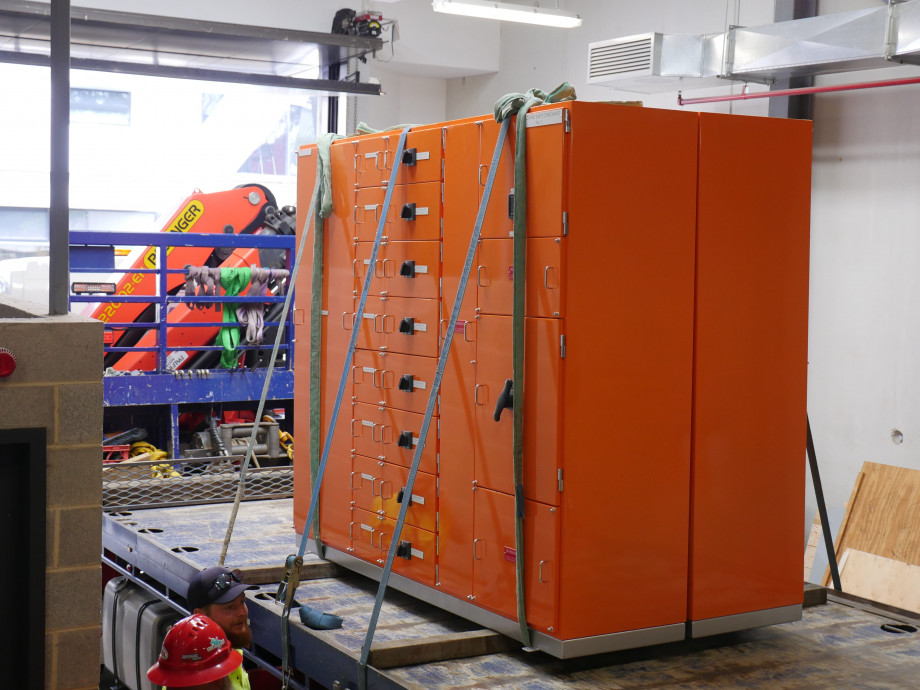 An orange metal box several metres wide and tall sits on the back of a flat bed truck.