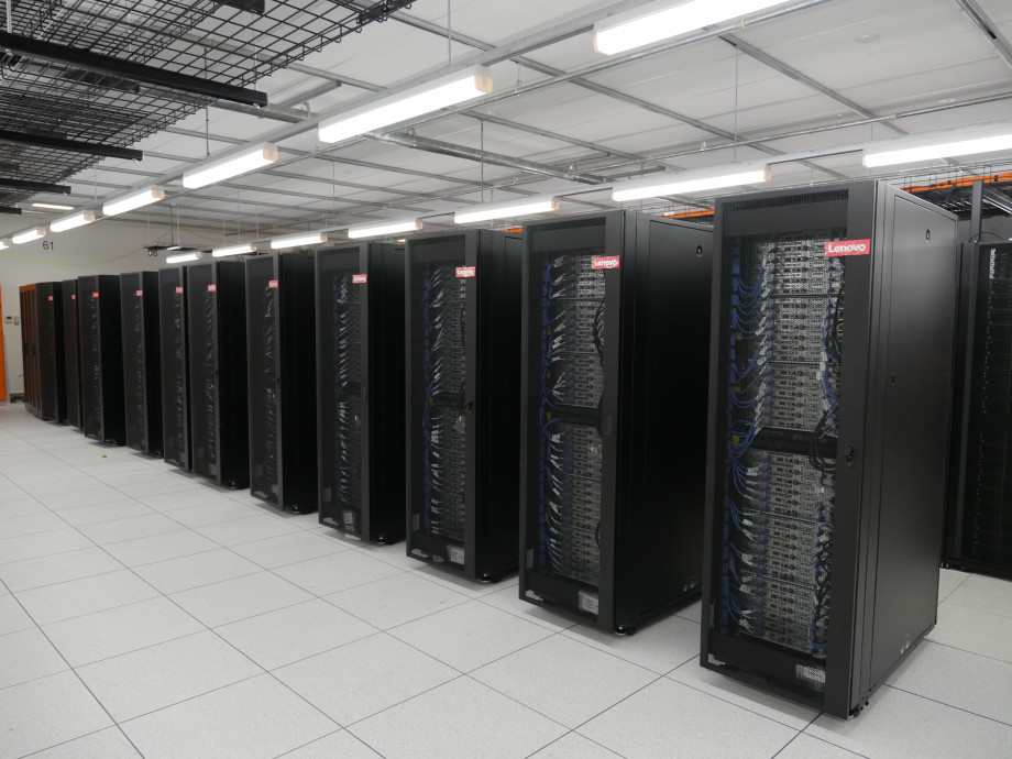 A long row of black and grey compute racks standing next to each other on a white floor.