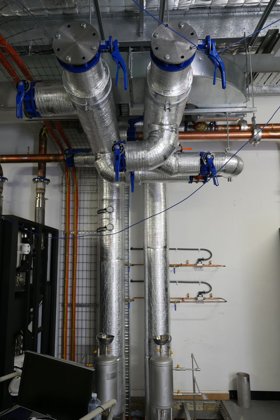 Two tall silver pipes with blue handles go up the wall and along the ceiling.