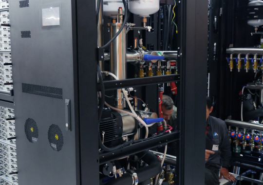 The exposed internal components of a water cooling system in a computer server rack, with visible pipes, tanks and pumps.