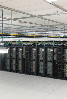 Wide picture of many rows of computer servers in a big open room, with blue artwork on one face.