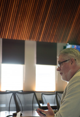 Professor Sean Smith seen close-up while talking during an official ceremony in a fancy boardroom. Logos and a banner are visible behind him.