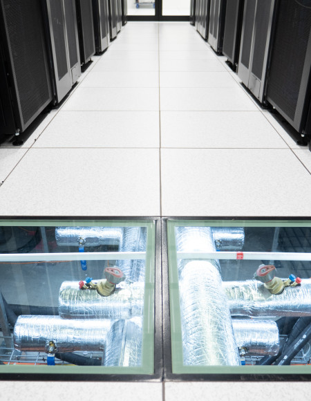 Clear floor tiles between two rows of tall black server racks reveal water pipes supplying cooling water for the Gadi supercomputer.