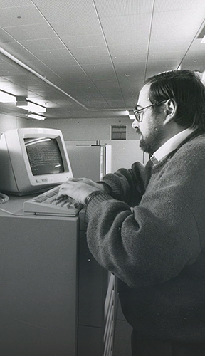 Black and white image of man operating old computer terminal
