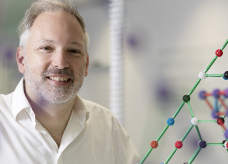 Professor Stephen Bartlett smiles at the camera with models of molecules around him.