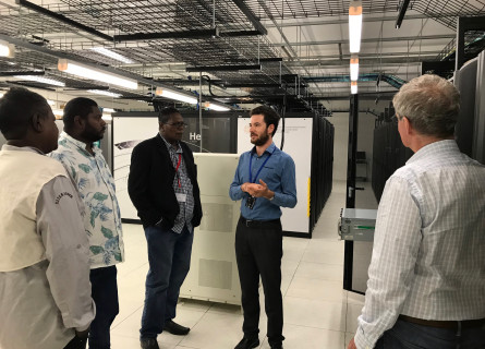 A group of Indigenous people standing with a tour guide giving them a tour of a supercomputer.