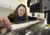 Nerilie Abram holds a long white object on a table, with large scientific equipment around her.