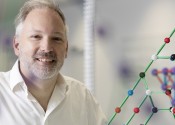 Professor Stephen Bartlett smiles at the camera with models of molecules around him.