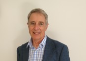 A smiling man, Dr Greg Ayers, in a blue suit and blue and white checkered shirt.