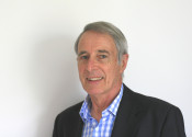 Greg Ayers, wearing a dark suit and blue and white shirt, smiles at the camera.