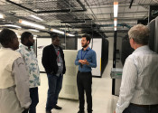A group of Indigenous people standing with a tour guide giving them a tour of a supercomputer.