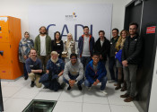 A group of a dozen people standing and crouching in front of a big sign on a wall reading GADI with some letters partially obscured.