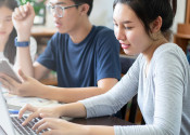 Three people working together on computing devices, with a gradient fading to grey on the left.